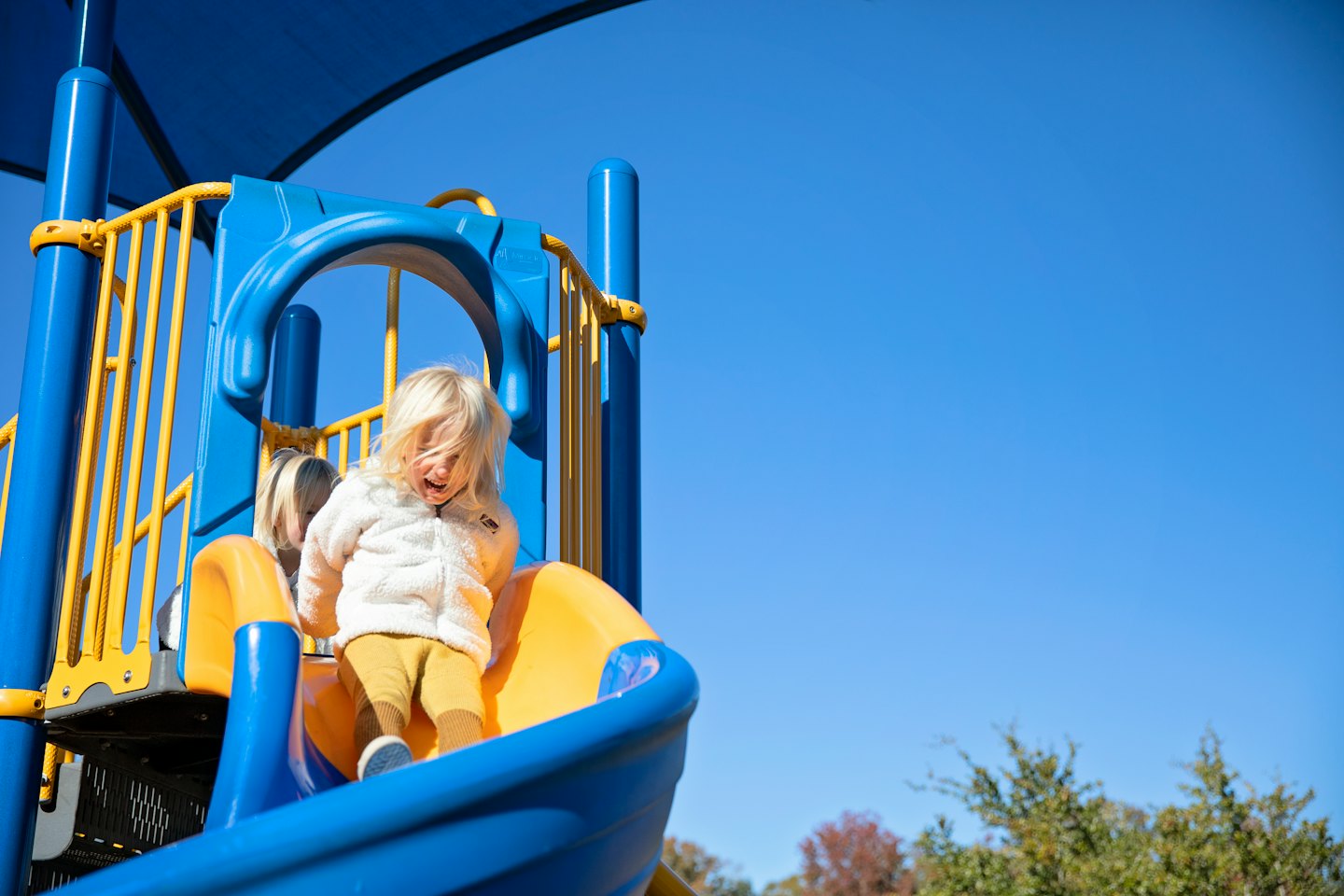 Kind lacht, während es eine bunte Rutsche auf dem Spielplatz hinunterrutscht.