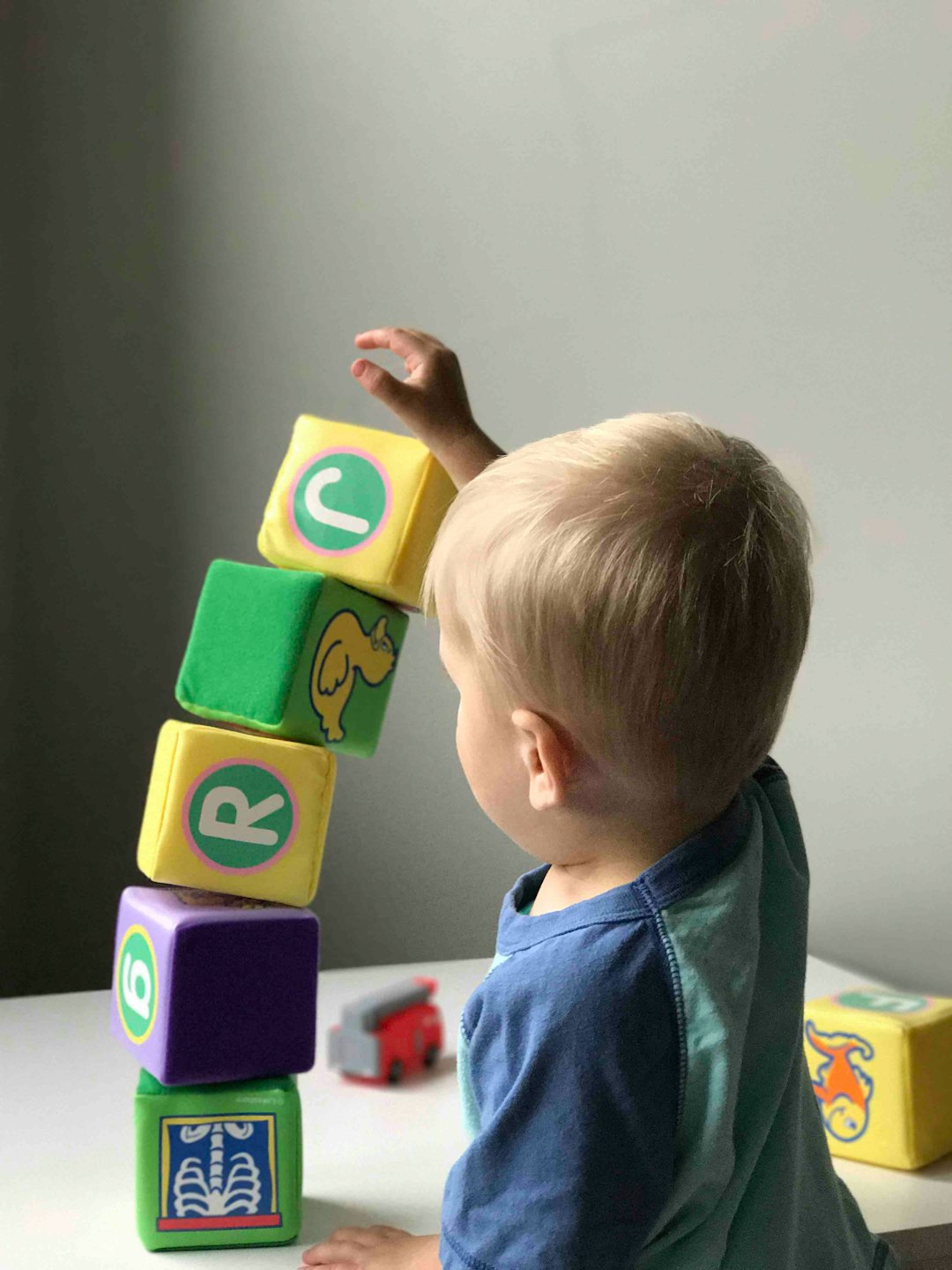 Kleinkind stapelt bunte Buchstaben- und Zahlenblöcke auf einem Tisch.